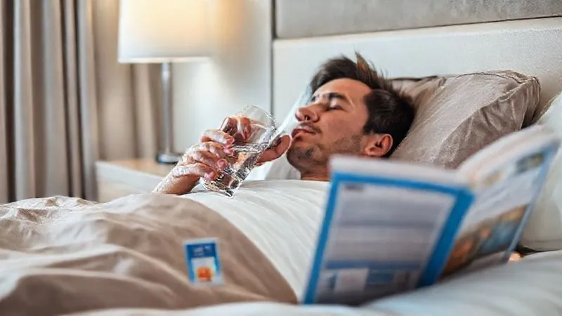 A photorealistic, professional photography, 8K, cinematic lighting, sharp focus, depth of field, shot on a high-end DSLR, showing a traveler resting comfortably in a clean hotel room, sipping from a glass of water with an ORS packet nearby, a travel guide open but unread, conveying a sense of calm recovery after a minor setback. A photorealistic, professional photography, 8K, cinematic lighting, sharp focus, depth of field, shot on a high-end DSLR, showing a traveler resting comfortably in a clean hotel room, sipping from a glass of water with an ORS packet nearby, a travel guide open but unread, conveying a sense of calm recovery after a minor setback.