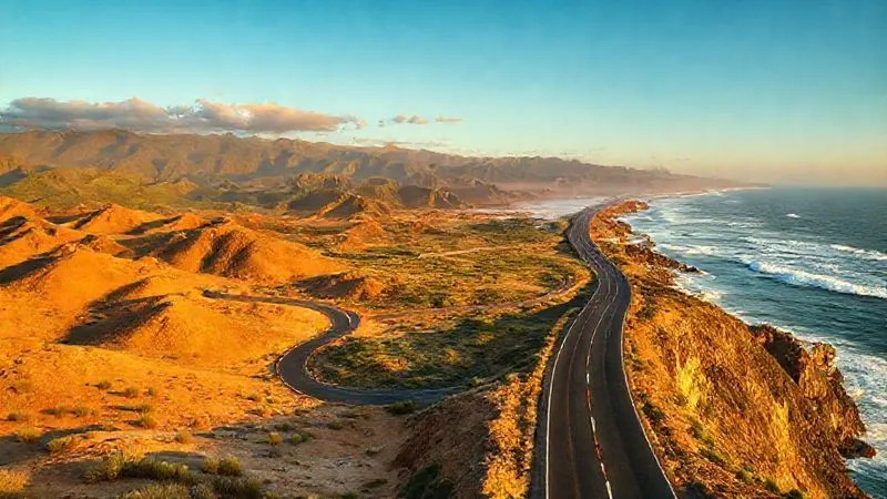 A breathtaking photorealistic panorama of diverse landscapes seamlessly transitioning: a winding desert road leading to lush green mountains, then merging into a coastal highway with crashing waves. The scene is bathed in golden hour light, suggesting a journey through varied terrains. Professional photography, 8K, cinematic lighting, sharp focus, depth of field, shot on a high-end DSLR.