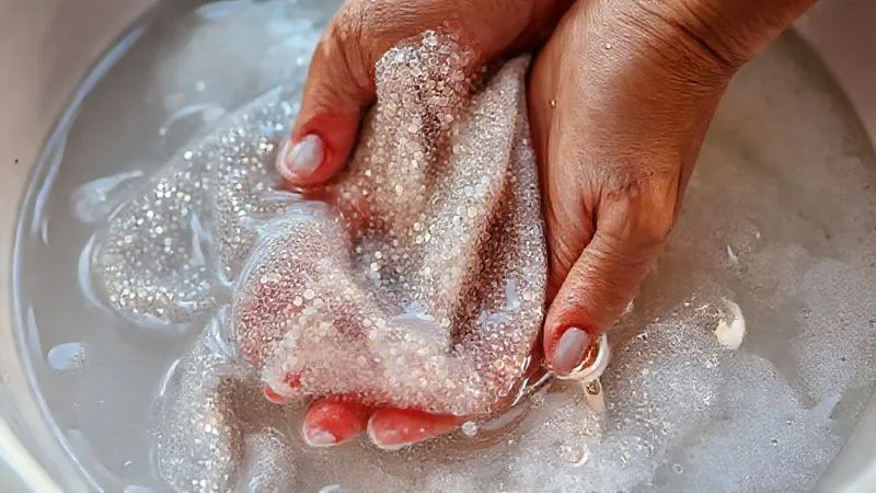 A close-up, photorealistic shot of delicate, sequined festival fabric being gently hand-washed in a basin of soapy water, with soft light reflecting off the sequins. The hands are careful and precise. Professional photography, 8K, cinematic lighting, sharp focus on the fabric and water, depth of field, shot on a high-end DSLR. A close-up, photorealistic shot of delicate, sequined festival fabric being gently hand-washed in a basin of soapy water, with soft light reflecting off the sequins. The hands are careful and precise. Professional photography, 8K, cinematic lighting, sharp focus on the fabric and water, depth of field, shot on a high-end DSLR.