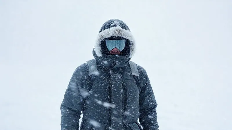 Photorealistic, professional photography, 8K, cinematic lighting, sharp focus, depth of field, shot on a high-end DSLR, depicting a lone figure, heavily bundled in winter gear, standing in a swirling, featureless whiteout. The ground, sky, and horizon are completely merged into a blinding white void, creating a strong sense of disorientation and isolation. The figure's face is barely visible, emphasizing the harshness of the environment.