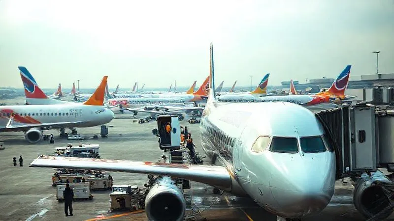 A crowded airport tarmac with multiple budget airline planes, one with a maintenance crew working on it, suggesting operational challenges and the tight scheduling of low-cost carriers. Photorealistic, professional photography, 8K, cinematic lighting, sharp focus, depth of field, shot on a high-end DSLR. A crowded airport tarmac with multiple budget airline planes, one with a maintenance crew working on it, suggesting operational challenges and the tight scheduling of low-cost carriers. Photorealistic, professional photography, 8K, cinematic lighting, sharp focus, depth of field, shot on a high-end DSLR.