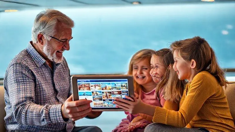 A photorealistic image of a diverse multi-generational family (grandparents, parents, children) smiling and looking at a tablet together, planning their cruise. The tablet screen shows a cruise ship itinerary with different age-group activities highlighted. Professional photography, 8K, cinematic lighting, sharp focus, depth of field. Shot on a high-end DSLR.
