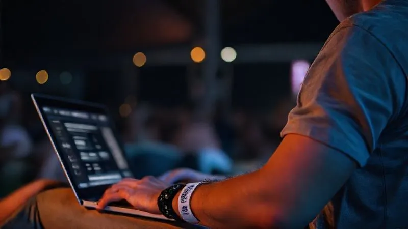 A person diligently researching festival safety and harm reduction strategies on a laptop, with a festival wristband on their arm, in a calm, well-lit setting, photorealistic, professional photography, 8K, cinematic lighting, sharp focus, depth of field, shot on a high-end DSLR.