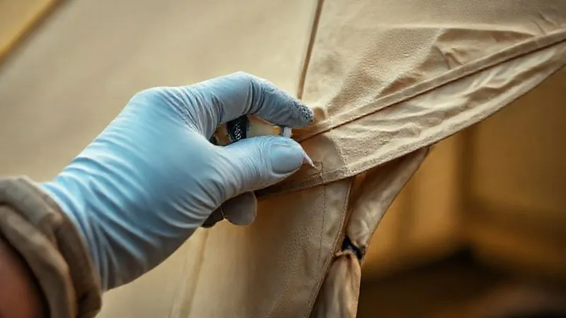 photorealistic, professional photography, 8K, cinematic lighting, sharp focus, depth of field, shot on a high-end DSLR, a close-up of a glamping tent seam being carefully re-sealed with a specialized sealant, showing attention to detail and professional maintenance. A gloved hand applies the product with precision, highlighting the proactive care involved in preserving luxury outdoor shelters.