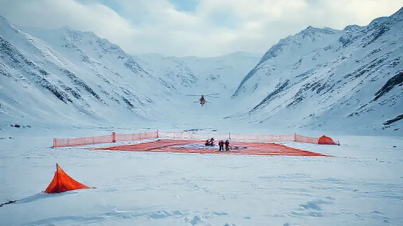 A photorealistic, professional photography, 8K, cinematic lighting, sharp focus, depth of field, shot on a high-end DSLR of a well-marked helicopter landing zone in a vast, snow-covered mountain valley. Bright orange tarps outline the clear area, with a small team standing ready. A rescue helicopter is visible in the distance, approaching the HLZ. The scene conveys readiness and coordination. A photorealistic, professional photography, 8K, cinematic lighting, sharp focus, depth of field, shot on a high-end DSLR of a well-marked helicopter landing zone in a vast, snow-covered mountain valley. Bright orange tarps outline the clear area, with a small team standing ready. A rescue helicopter is visible in the distance, approaching the HLZ. The scene conveys readiness and coordination.