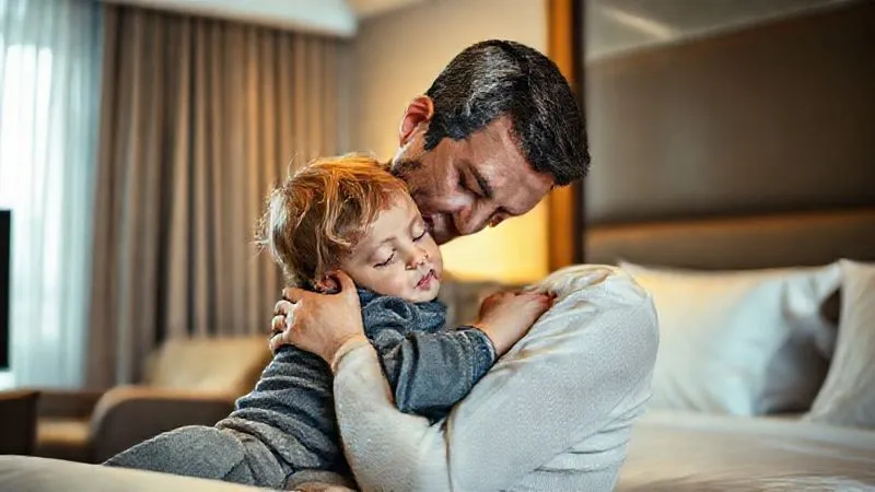 A photorealistic, professional photography, 8K, cinematic lighting, sharp focus, depth of field, shot on a high-end DSLR, capturing a tender moment between a professional parent and their toddler in a hotel room. The parent is gently hugging or comforting the child, who looks sleepy but content. The scene is warm and intimate, with soft light, conveying emotional support and bonding amidst travel challenges. A photorealistic, professional photography, 8K, cinematic lighting, sharp focus, depth of field, shot on a high-end DSLR, capturing a tender moment between a professional parent and their toddler in a hotel room. The parent is gently hugging or comforting the child, who looks sleepy but content. The scene is warm and intimate, with soft light, conveying emotional support and bonding amidst travel challenges.