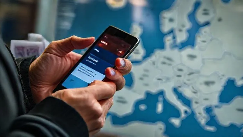 A photorealistic professional photography shot of a traveler's hands holding a smartphone displaying a train app with a delay notification, while the other hand clutches a physical train ticket. A blurred map of Europe is visible in the background. 8K, cinematic lighting, sharp focus on hands and phone, depth of field, shot on a high-end DSLR. A photorealistic professional photography shot of a traveler's hands holding a smartphone displaying a train app with a delay notification, while the other hand clutches a physical train ticket. A blurred map of Europe is visible in the background. 8K, cinematic lighting, sharp focus on hands and phone, depth of field, shot on a high-end DSLR.